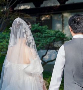 웨딩드레스와 하얀 베일을 쓴 신부와 예복 정장을 입은 신랑의 뒷모습, 20대 후반 신혼부부의 순조로운 결혼 준비 과정과 예식을 상징하는 풍경