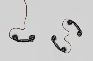 하얀 바닥 위에 거치대 없이 놓여 있는 두 개의 검은색 전화 수화기 모습, 오래된 연인 사이에서 발생하는 연락 소홀과 소통의 부재로 인해 깊어지는 서운함을 표현한 풍경