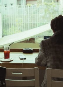 창밖이 내다보이는 테이블에 홀로 앉아 노트북을 바라보는 사람의 뒷모습, 기혼 직장상사와의 사적인 관계 속에서 끊임없이 밀려오는 불안감과 내면의 고민을 표현한 모습