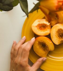 노란 접시에 담긴 잘린 복숭아들과 그 곁에 놓인 사람의 손 구도, 황도 안주 가성비 논란을 통해 외식비 지출 기준을 엄격하게 재점검하는 소비자 트렌드를 표현한 모습