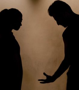 어두운 조명 아래 마주 보고 서서 손짓으로 갈등을 표현하는 남녀의 실루엣 모습, 고부갈등 상황에서 가까운 가족의 말 한마디가 주는 깊은 상처와 마음에 남는 이유를 표현한 풍경