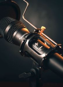 스튜디오 스탠드에 거치된 검은색 마이크의 근접 모습, 아티스트의 사회적 논란과 음악적 결과물 소비를 분리해서 볼 것인가에 대한 대중의 상반된 인식을 표현한 모습